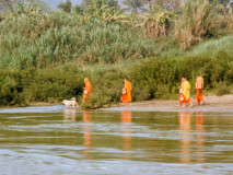 Monges budistas com vestes laranja caminhando ao longo do rio Mekong no norte do Laos, vistos durante a viagem de slow boat entre Luang Prabang e Huay Xai